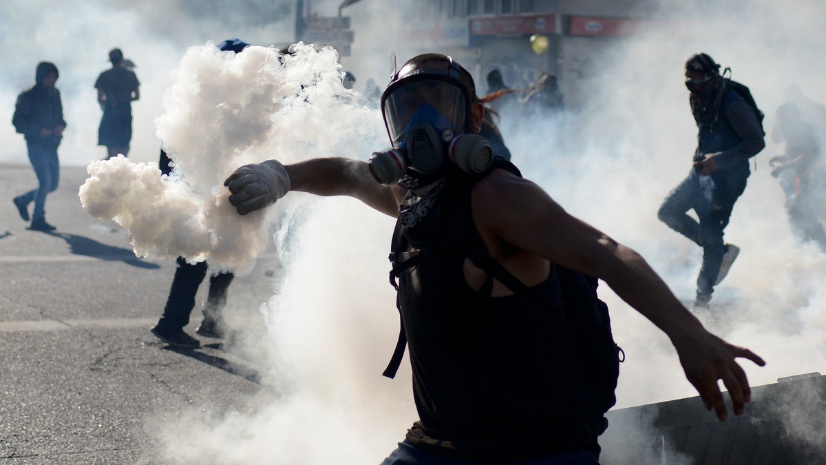 An anti-government protester returns a tear gas canister to police during clashes in Valparaiso, Chile, Friday, Oct. 25, 2019. A new round of clashes broke out Friday as demonstrators returned to the streets, dissatisfied with economic concessions announced by the government in a bid to curb a week of deadly violence.(AP Photo/Matias Delacroix)