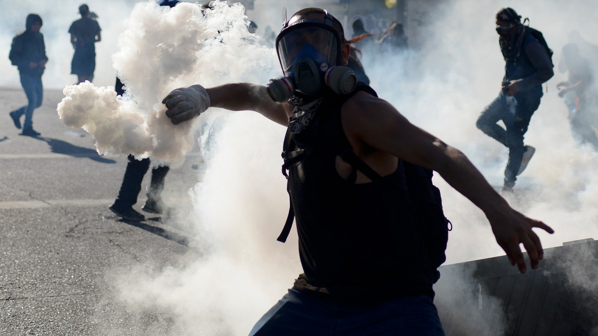 An anti-government protester returns a tear gas canister to police during clashes in Valparaiso, Chile, Friday, Oct. 25, 2019. A new round of clashes broke out Friday as demonstrators returned to the streets, dissatisfied with economic concessions announced by the government in a bid to curb a week of deadly violence.(AP Photo/Matias Delacroix)