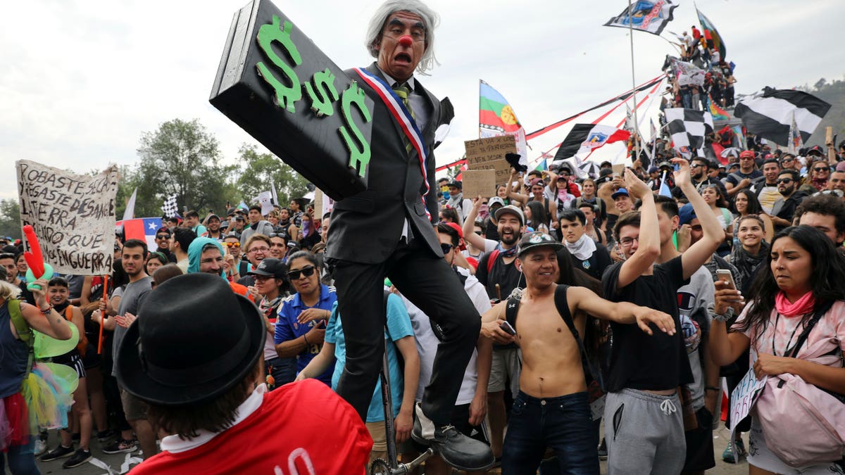 An artist performs as Chile's President Sebastian Pinera holding a briefcase embellished with dollars signs, during an anti-government protest in Santiago, Chile, Friday, Oct. 25, 2019. At least 19 people have died in the turmoil that has swept the South American nation. The unrest began as a protest over a 4-cent increase in subway fares and soon morphed into a larger movement over growing inequality in one of Latin America's wealthiest countries. (AP Photo/Rodrigo Abd)