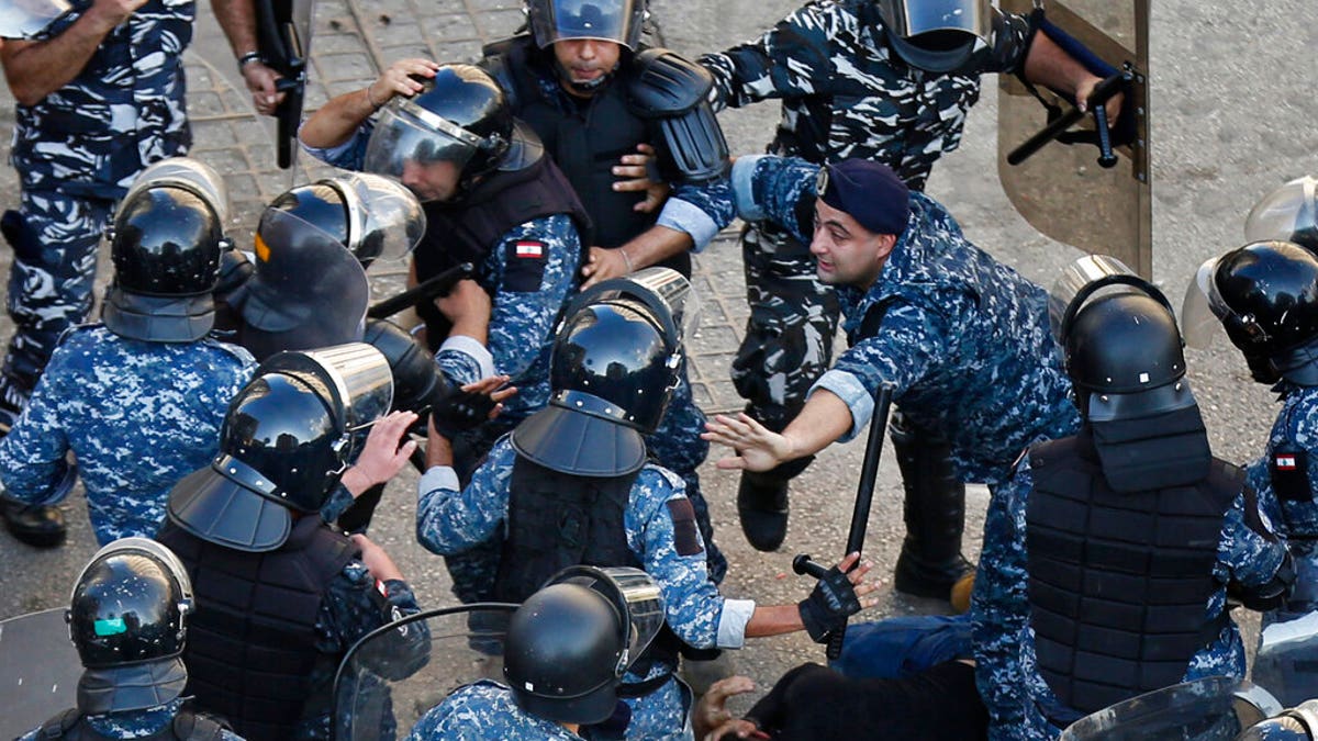 A riot police officer, center right, stops other policemen from beating a protester who lies on the ground, after clashes erupted between an anti-government protesters and Hezbollah supporters near the government palace, in Beirut, Lebanon, Tuesday, Oct. 29, 2019. 