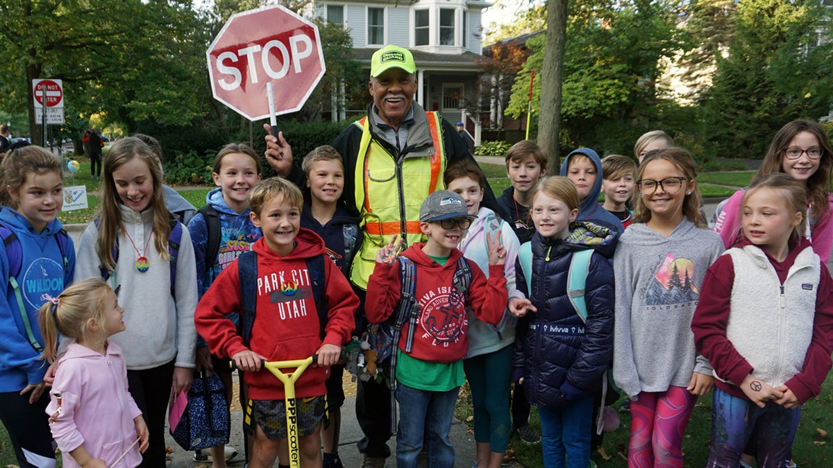 Alec Childress, 80, poses with school children he helps as a crossing guard in Illinois. On Thursday, his birthday, they surprised him with a big celebration to thank him for brightening their day every morning.