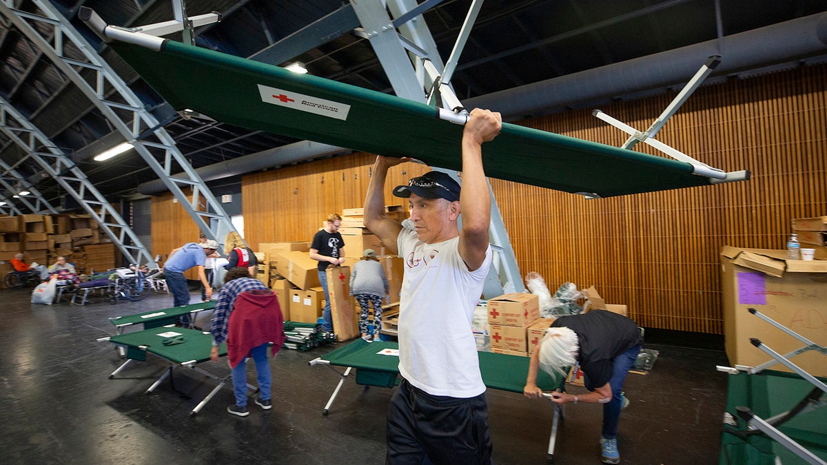 In this Sunday, Oct. 27, 2019, photo, volunteer Alejandro Pablo carries a newly built cot to an evacuee in need at a Red Cross shelter set up for wildfire evacuees at the Sonoma County Fairgrounds in Santa Rosa, Calif.
