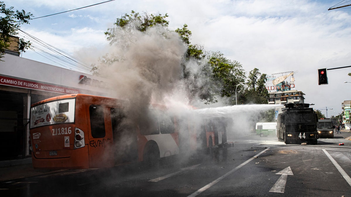 A police water cannon extinguishes a burning bus that was set alight by demonstrators during a protest in Santiago, Chile, Saturday, Oct. 19, 2019.