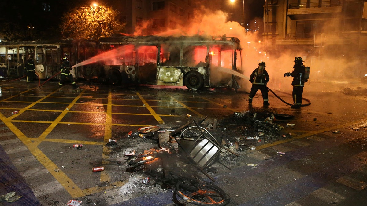 Firefighters put out the flames on a burning bus during a protest against the rising cost of subway and bus fares, in Santiago, Friday, Oct. 18, 2019.