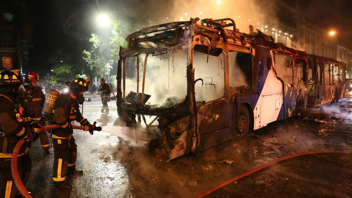 Firefighters put out the flames on a burning bus during a protest against the rising cost of subway and bus fares, in Santiago, Friday, Oct. 18, 2019.