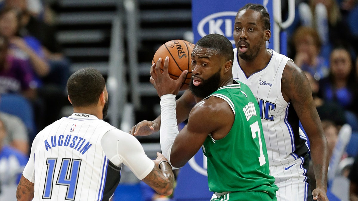 Boston Celtics' Jaylen Brown, center, looks to pass the ball as he is guarded by Orlando Magic's D.J. Augustin (14) and Al-Farouq Aminu , right, during the first half of an NBA preseason basketball game, Friday, Oct. 11, 2019, in Orlando, Fla. (AP Photo/John Raoux)