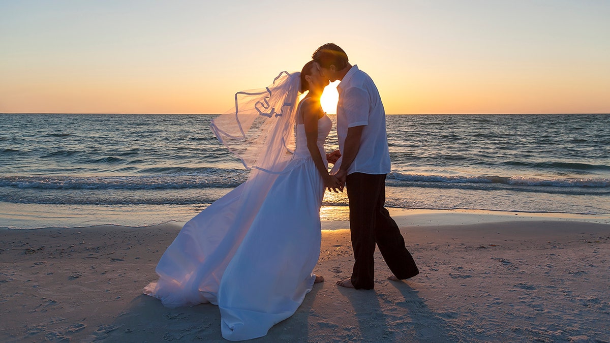 A married couple, bride and groom, kissing at sunset or sunrise on a beautiful tropical beach (Photo: iStock)