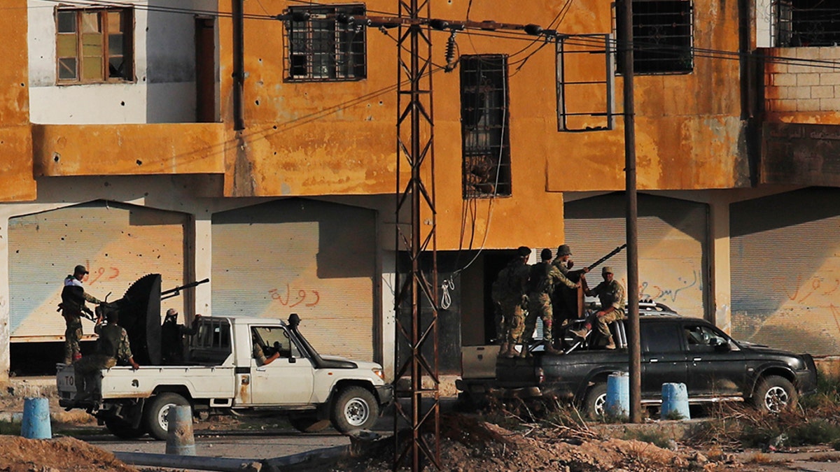 In this photo taken from the Turkish side of the border between Turkey and Syria, in Akcakale, Sanliurfa province, southeastern Turkey, Turkish-backed Syrian opposition fighters on pick-up trucks drive in Tal Abyad, Syria, Sunday, Oct. 13, 2019. State-run Anadolu news agency reported Tal Abyad had fallen to a Turkish military offensive on Sunday. Even after the announcement, sporadic gunfire and the occasional mortar round could still be heard in the town, which is on the border with Turkey, while smoke could be seen rising from several points in the town. (AP Photo/Cavit Ozgul)