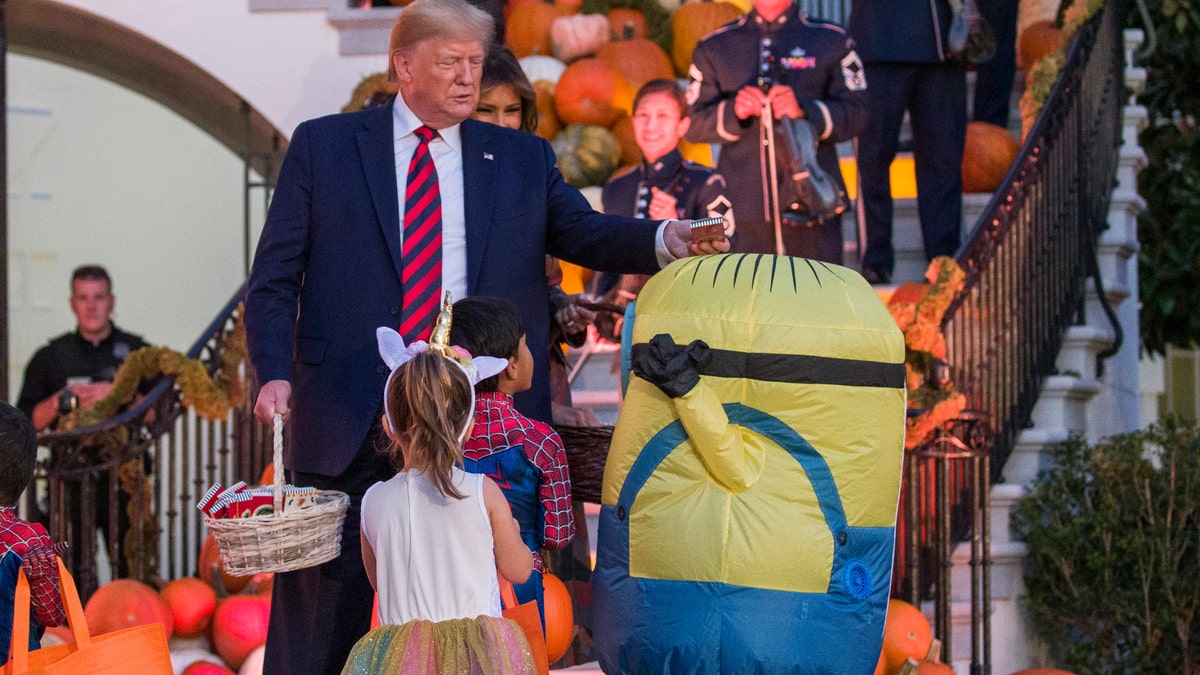 President Donald Trump, accompanied by first lady Melania Trump, places a candy bar on the head of child dressed as Minion during a Halloween trick-or-treat event on the South Lawn of the White House, which is decorated for Halloween, on Monday, Oct. 28, 2019.
