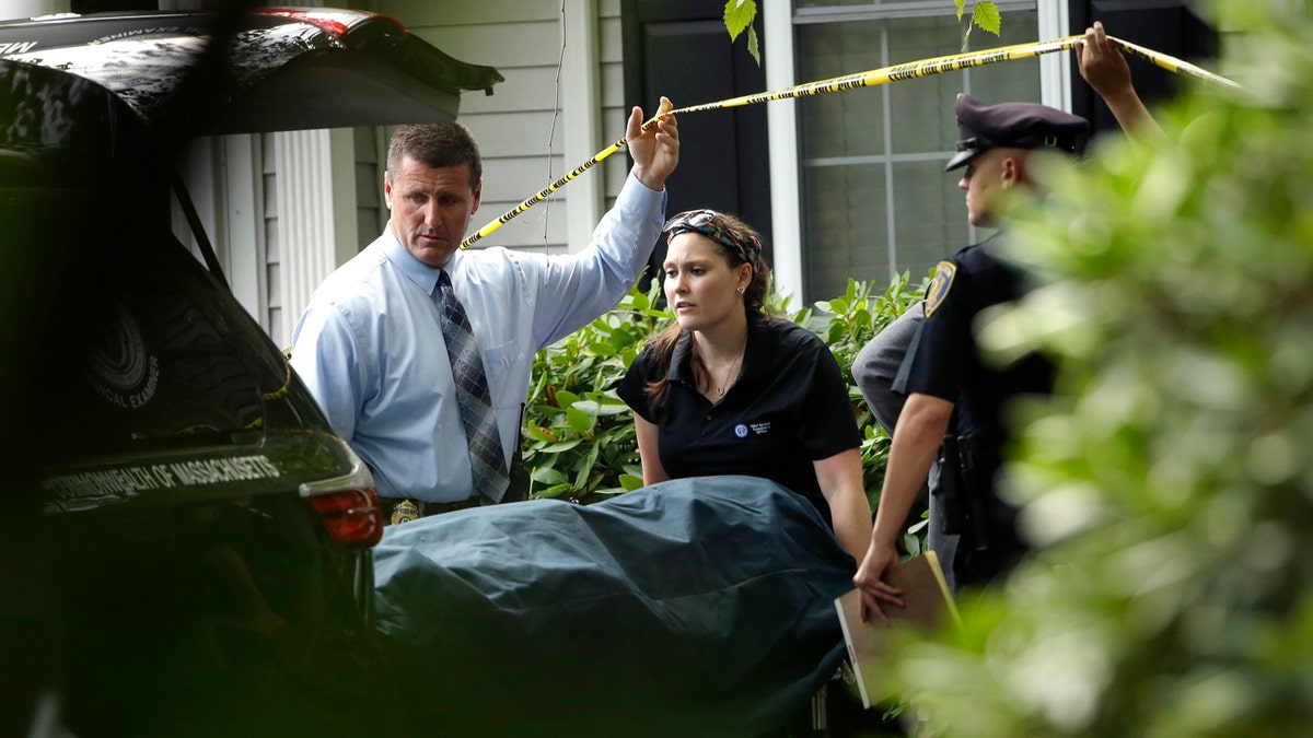 A woman from the Massachusetts Chief Medical Examiners Office, center, uses a gurney to place human remains into a vehicle as law enforcement officers hold caution tape at a home where two adults and three children were found dead with gunshot wounds, Monday, Oct. 7, 2019, in Abington, Mass. (AP Photo/Steven Senne)