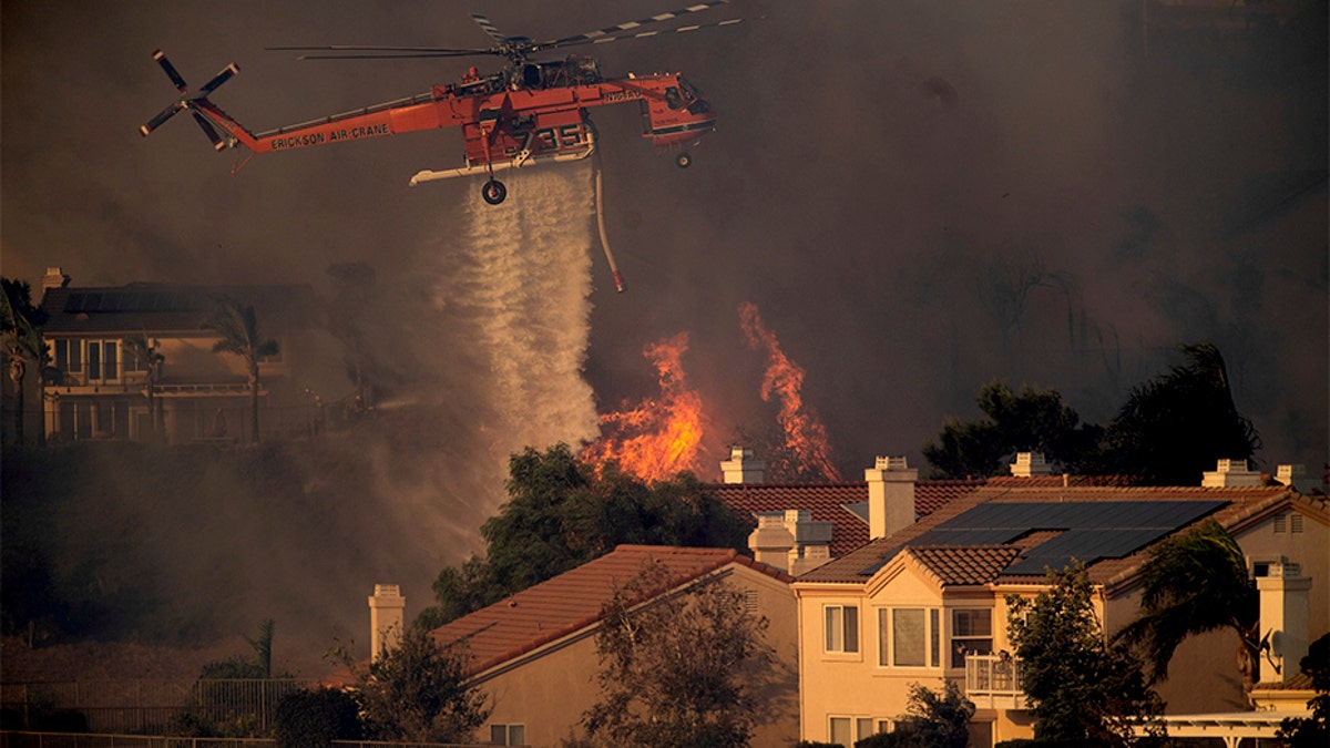 A helicopter drops water while battling the Saddleridge fire in Porter Ranch, Calif., on Friday. (AP)