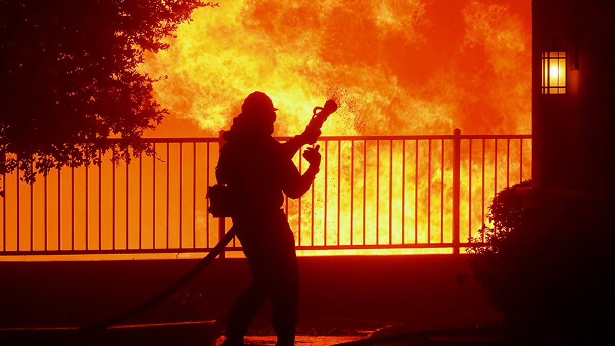 A firefighter waits for water as the Saddleridge fire flares up near homes in Sylmar, Calif.