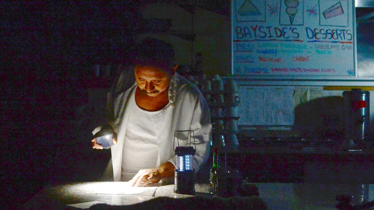 Carlos Lama of Bayside Cafe, which was among businesses to lose power due to PG&amp;E's public safety power shutoff, uses an LED lamp and light from his phone at the counter of the restaurant in Sausalito, Calif. (Alan Dep/Marin Independent Journal via AP)