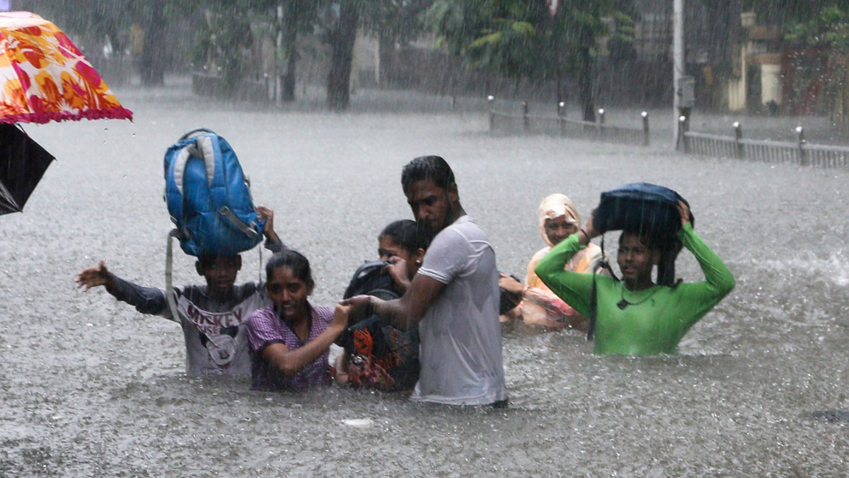 FILE - In this Sept. 4, 2019, file photo, people hold hands and navigate their way through a flooded street as it rains in Mumbai, India. The number of people threatened by climate change-triggered flooding is about three times higher than previously thought, a new study says. But it's not because of more water. It's because the land, especially in Asia and the developing world, is several feet lower than what space-based radar has calculated, according to a study in the journal Nature Communications Tuesday, Oct. 29. (AP Photo/Rajanish Kakade, File)