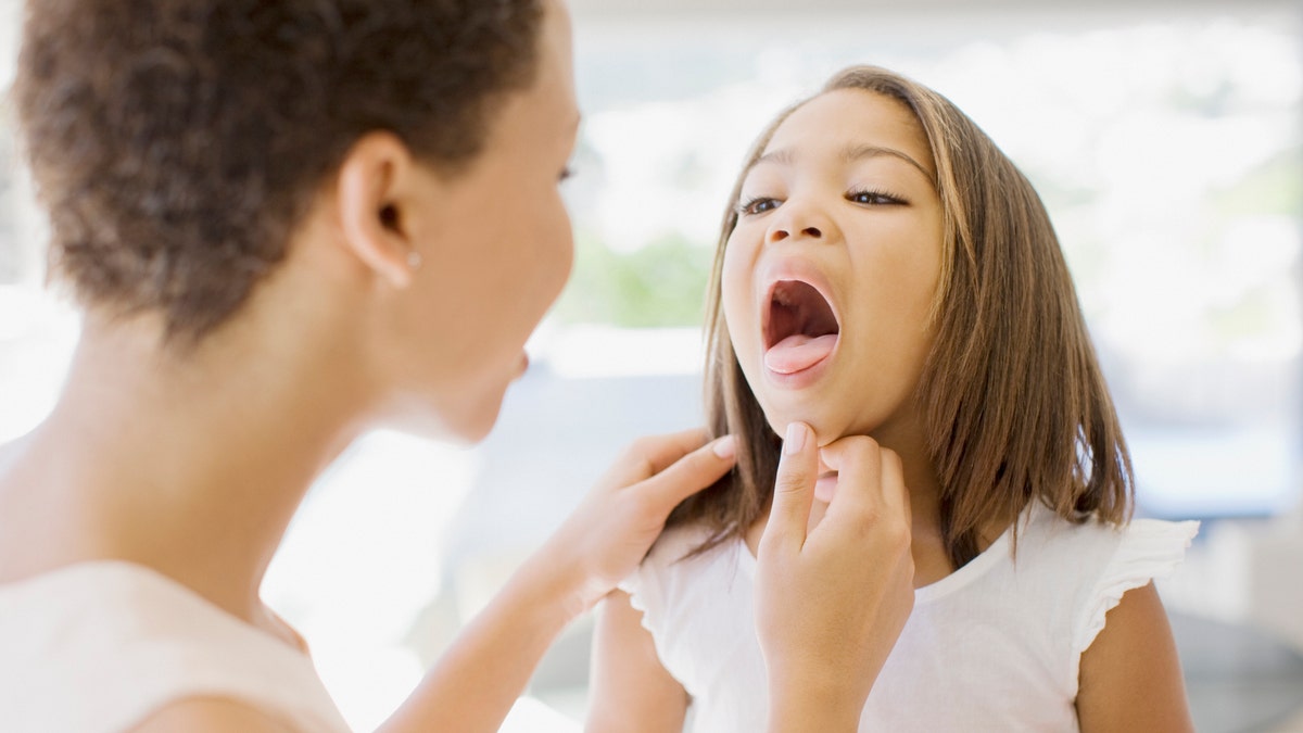 woman looks down child's throat