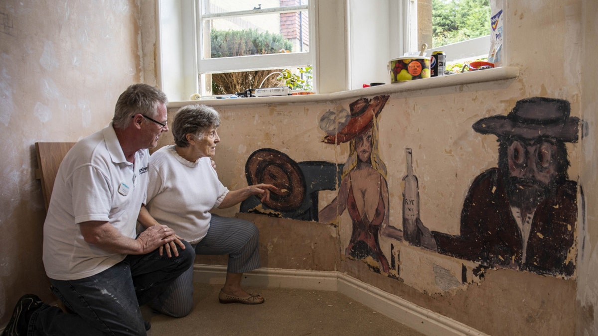 David Parton a staff member at Stokeleigh Care Home who discovered a series of paintings believed to date back to World War II shows them to Jan, a resident at the Care Home. Due to the picture's "racy" nature, it is believed the room may have been used as a gentlemen's lounge. (Credit: SWNS)