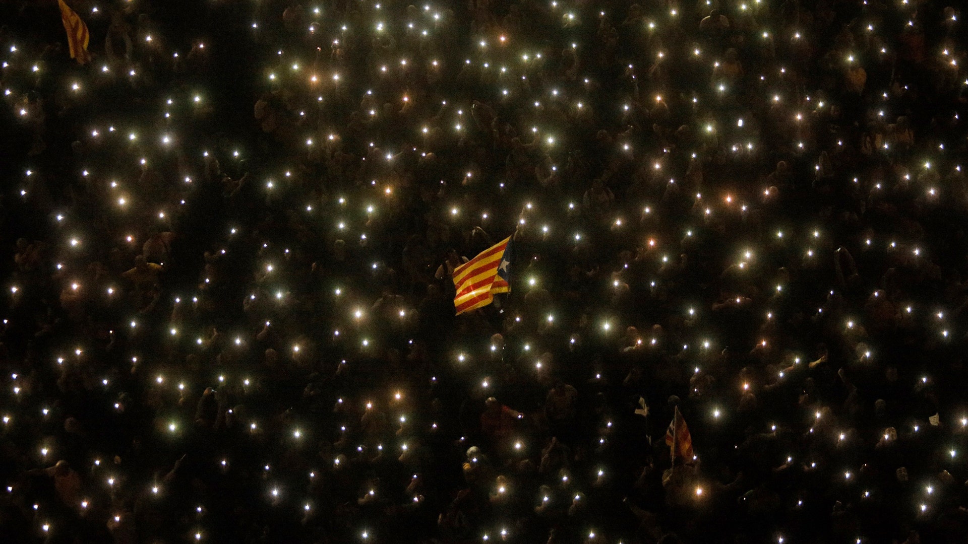 A Catalonian independence flag is waved as people hold up their phones with the flashlight switched on during a Catalan pro-independence protest in Barcelona, Spain, Oct. 20, 2019. 