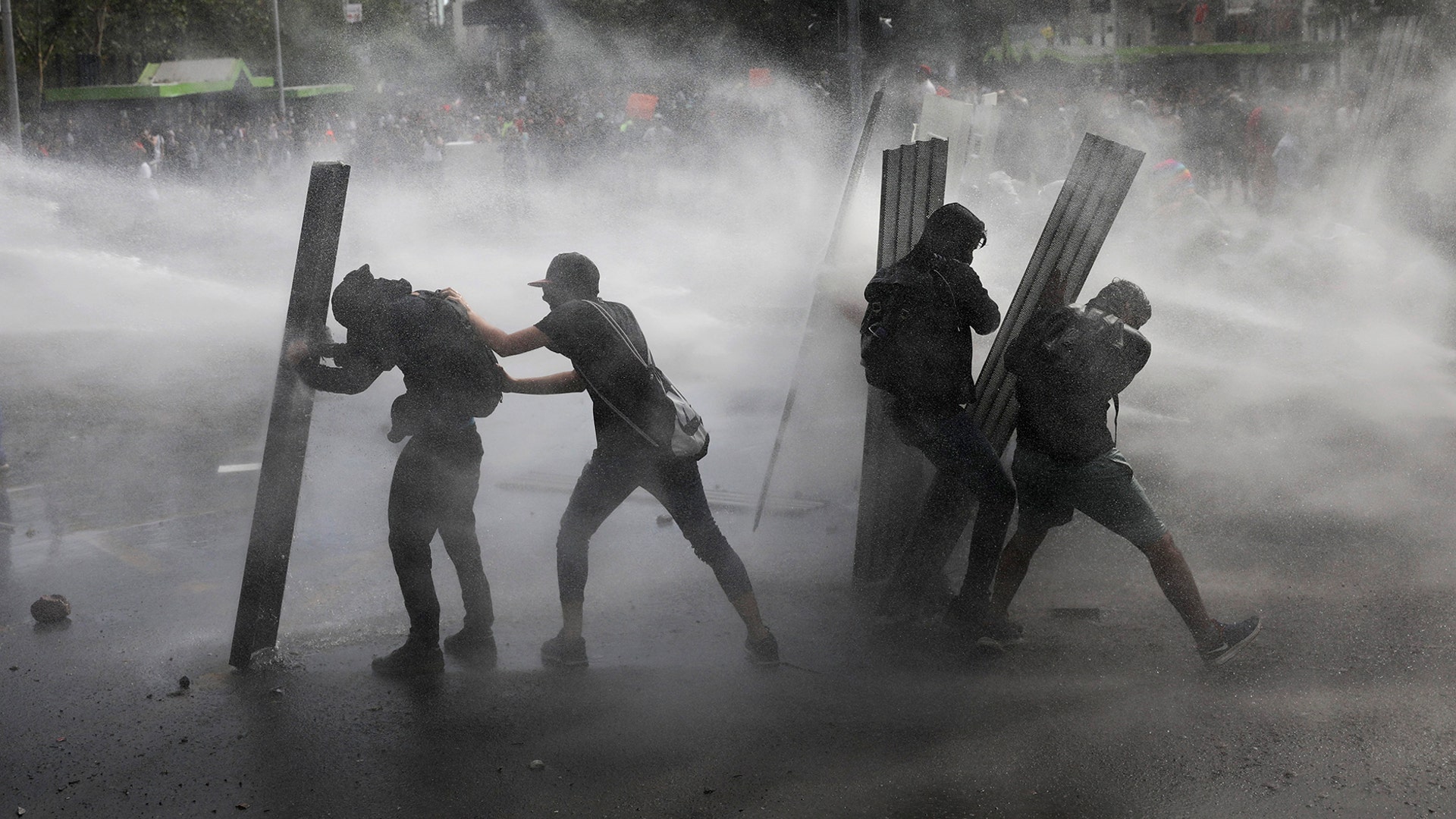 Anti-government demonstrators brace themselves behind shields as they're sprayed with a police water cannon in Santiago, Chile, Oct. 22, 2019. 