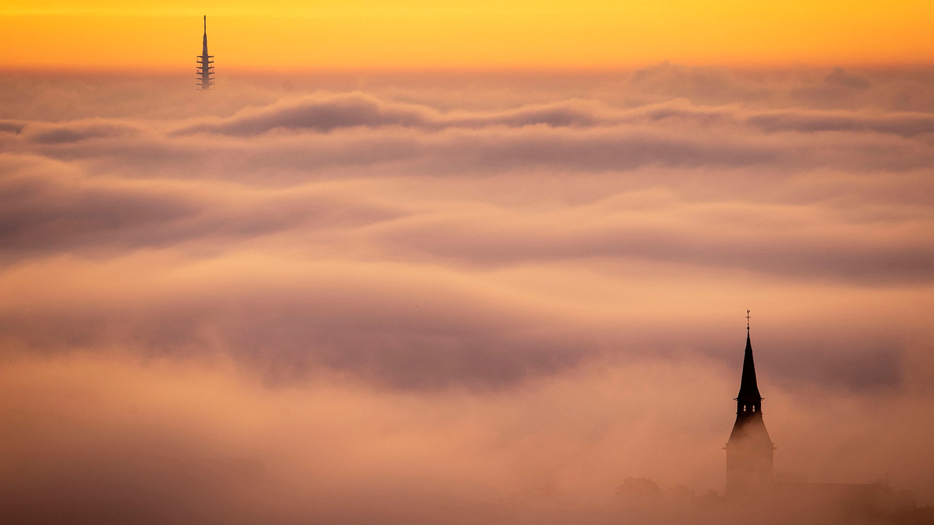 The church tower of Kronberg and Frankfurt's television tower rise through the fog as the sun rises over Frankfurt, Germany, Oct. 26, 2019. 