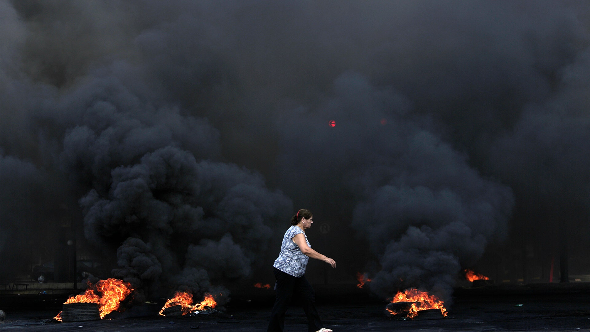A woman walks by burning tires that were set fire to block a road during a protest against the government's plans to impose new taxes in Beirut, Lebanon, Oct. 18, 2019. 