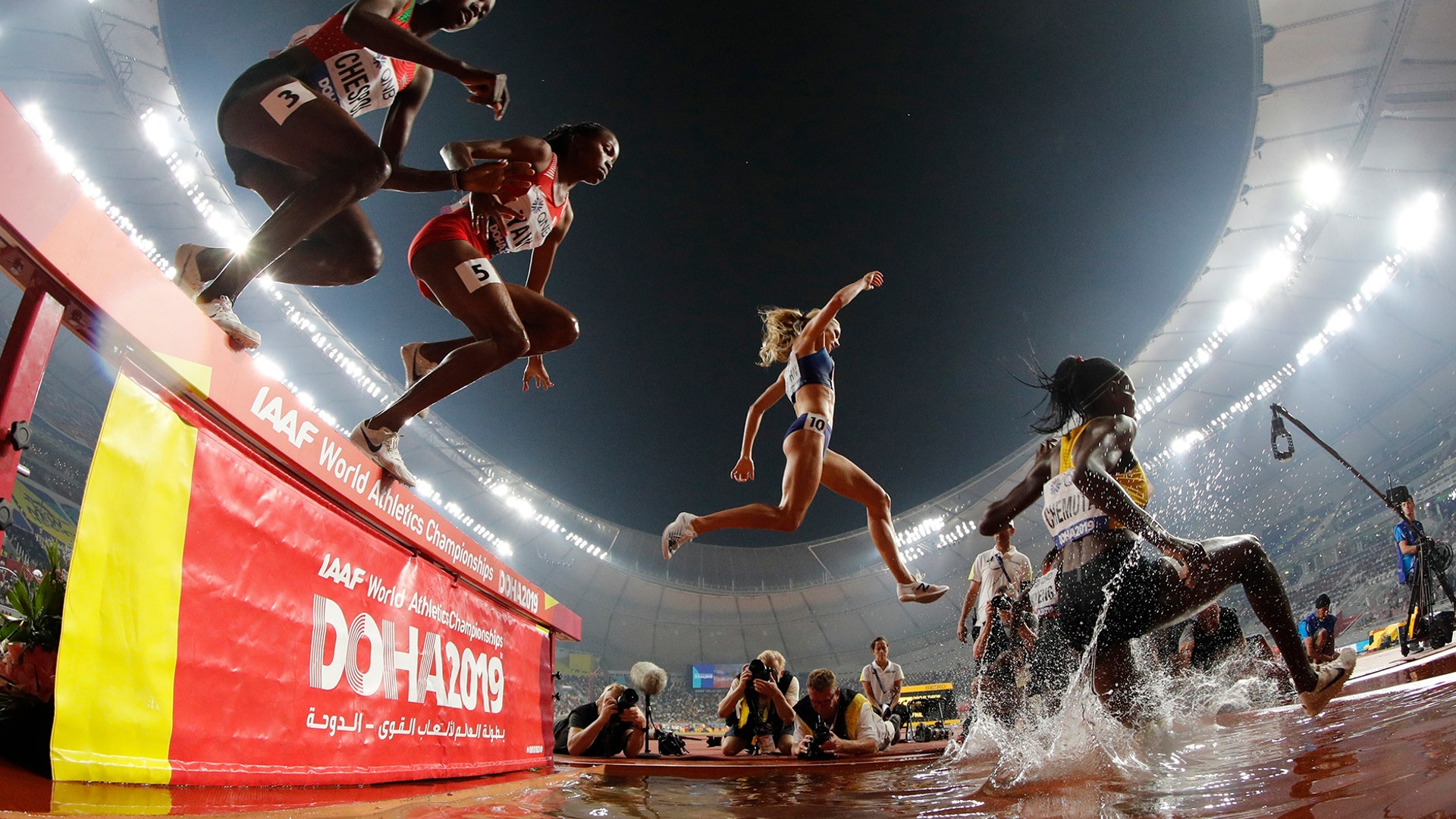 Competitors in the women's 3000-meter steeplechase final run through a water jump at the World Athletics Championships in Doha, Qatar, Sept. 30, 2019. 