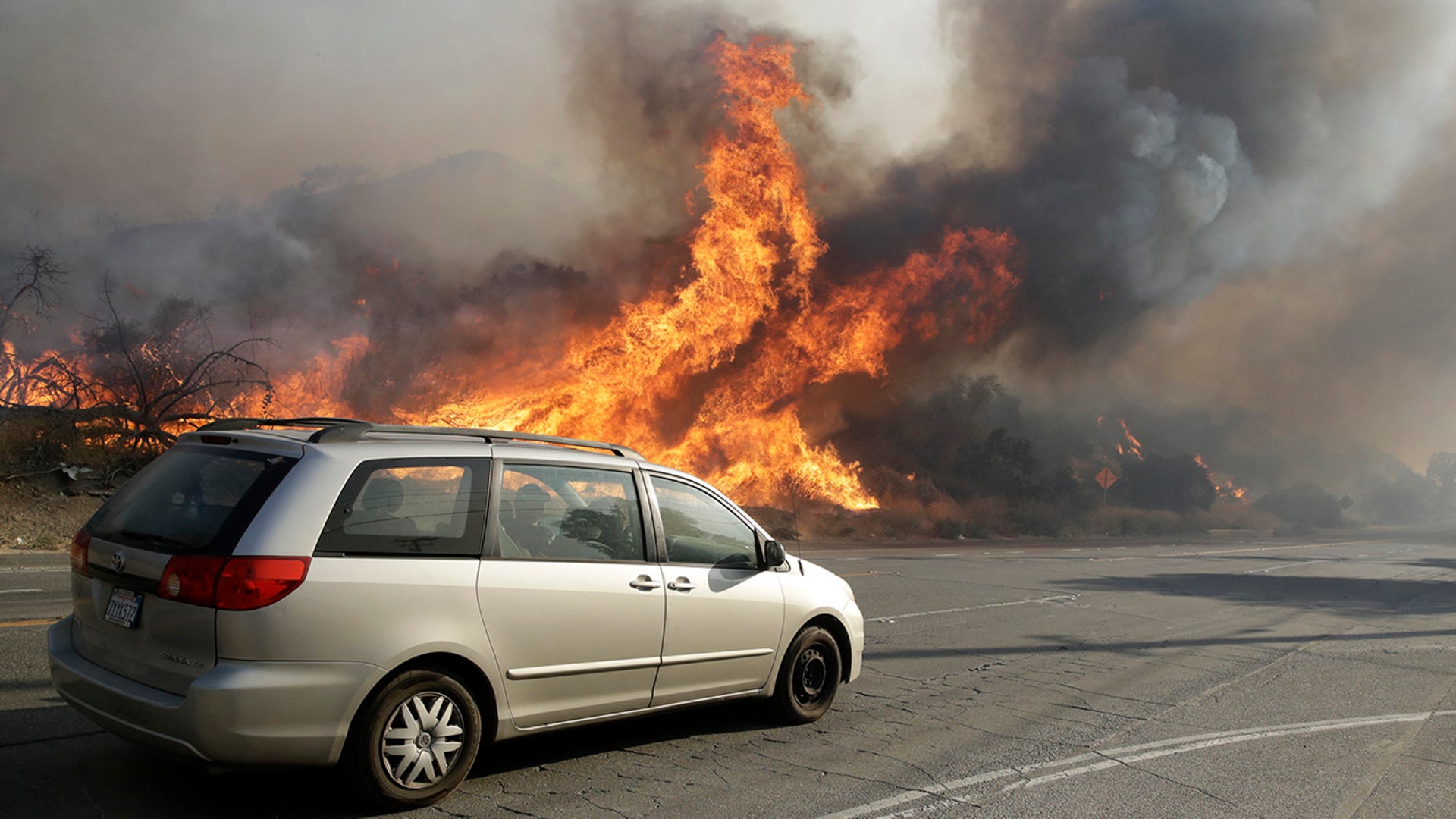 Traffic continues to flow along Sierra Highway as flames from a wildfire are close by Thursday, Oct. 24, 2019, in Santa Clarita, Calif. (AP Photo/Marcio Jose Sanchez)
