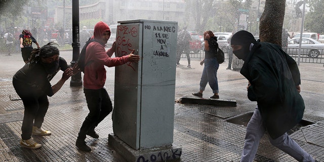 Demonstrators run for cover from a police water cannon during a protest in Santiago, Chile, Saturday, Oct. 19, 2019. (Associated Press)