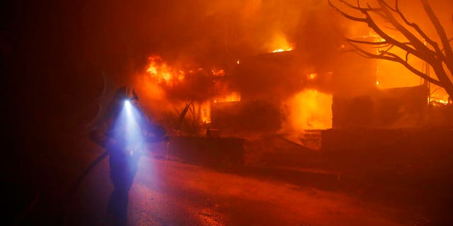 A firefighters gets in position to hose down flames as a home burns in the Getty fire area along Tigertail Road, Oct. 28, 2019, in Los Angeles. (AP Photo/Marcio Jose Sanchez)