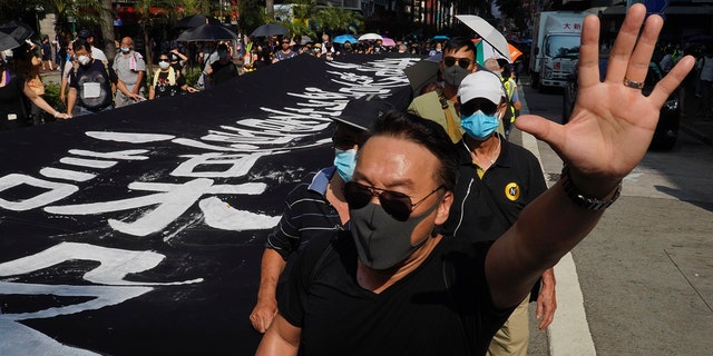A masked protester holds up his hand to represent the protesters' five demands as he walks next to a banner reading "Hong Kong police deliberately murder" in Hong Kong on Saturday, Oct. 5, 2019. All subway and trains services are closed in Hong Kong after another night of rampaging violence that a new ban on face masks failed to quell. (AP Photo/Vincent Yu)