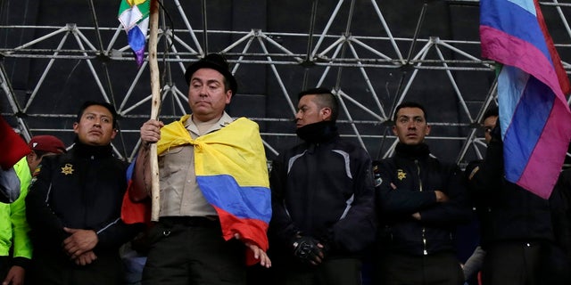 A policeman detained by anti-government protesters is made to hold an indigenous banner while standing on a stage in Quito, Ecuador, on Thursday. (AP Photo/Dolores Ochoa)