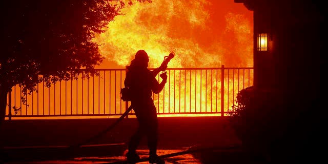 In this Thursday, Oct. 10, 2019 photo, a firefighter waits for water as the Saddleridge fire flares up near homes in Sylmar, Calif. (Associated Press)