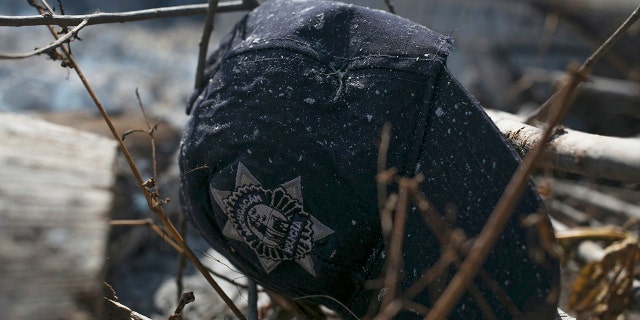 The cap of a Michoacan state police officer lies in the brush where charred police trucks stand on the roadside after its police officer occupants were attacked in El Aguaje, Mexico, Monday, Oct. 14, 2019.