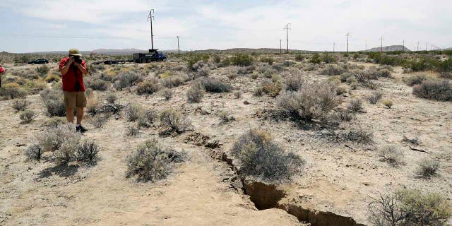 FILE - In this July 7, 2019 file photo, a visitor takes a photo of a crack in the ground following recent earthquakes near Ridgecrest, Calif. (AP Photo/Marcio Jose Sanchez, File)