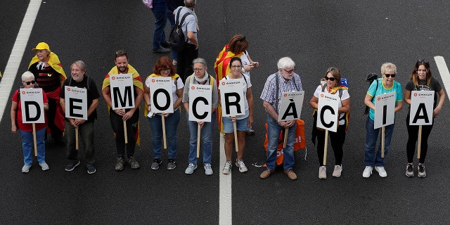 Protesters march with a letters reading 'Democracy' on the fifth day of protests over the conviction of a dozen Catalan independence leaders in Barcelona, Spain, Friday, Oct. 18, 2019.