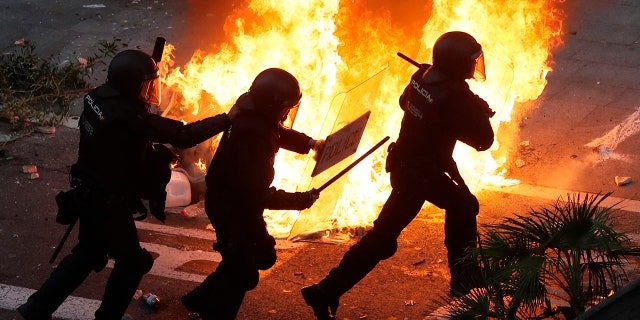 Police officers run past a burning barricade on the fifth day of protests over the conviction of a dozen Catalan independence leaders in Barcelona, Spain, Friday, Oct. 18, 2019. (AP Photo/Manu Fernandez)