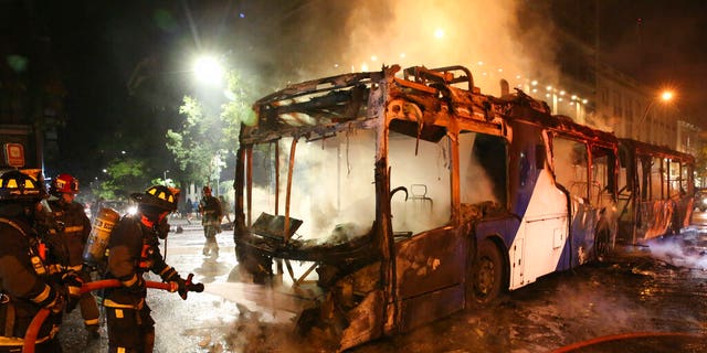 Firefighters put out the flames on a burning bus during a protest against the rising cost of subway and bus fares, in Santiago, Friday, Oct. 18, 2019. 