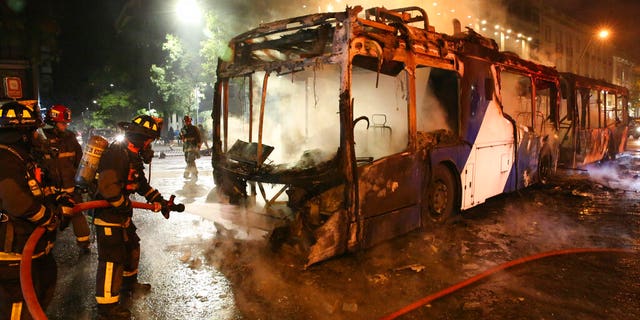 Firefighters put out the flames on a burning bus during a protest against the rising cost of subway and bus fares, in Santiago, Friday, Oct. 18, 2019.