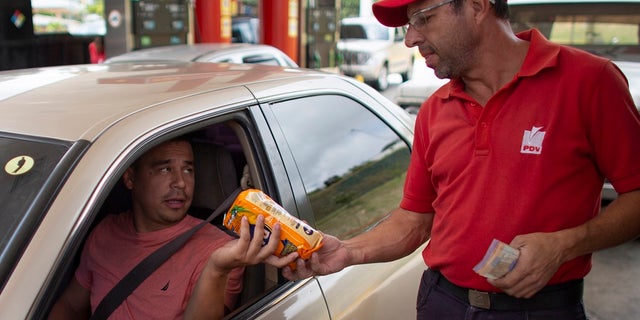 In this Oct. 8, 2019 photo, gas station attendant Orlando Godoy takes a package of corn flour as payment after filling a motorist's tank, which costs a tiny fraction of a U.S. penny, in San Antonio de los Altos on the outskirts of Caracas, Venezuela. The economy is in such shambles that drivers are now paying for fill-ups with a little food, a candy bar or just a cigarette. (AP Photo/Ariana Cubillos)