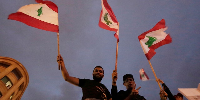 Hezbollah supporters wave Lebanese national flag as Lebanese riot policemen separate them from anti-government protesters during a protest in Beirut, Lebanon, Thursday, Oct. 24, 2019. Lebanon's President Michel Aoun has told tens of thousands of protesters that an economic reform package put forth by the country's prime minister will be the "first step" toward saving Lebanon from economic collapse. (AP Photo/Hassan Ammar)