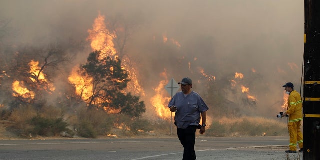 A man walks along Sierra Highway as flames from a wildfire overtake a hillside Thursday, Oct. 24, 2019, in Santa Clarita, Calif. The flames are fed by dry winds that are predicted to strengthen throughout the day across the region. (AP Photo/Marcio Jose Sanchez)