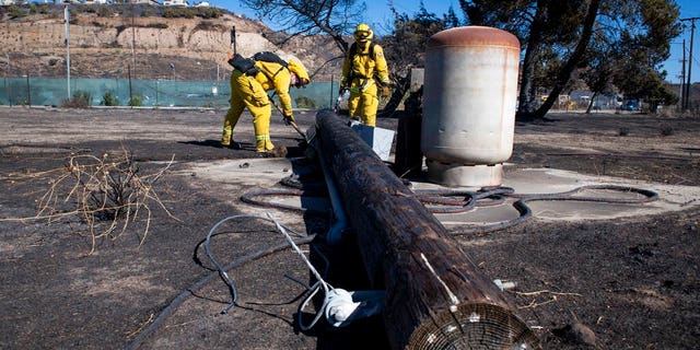 Firefighters with Cal Fire examine a burned down low voltage power pole during the Tick Fire, Thursday, Oct. 25, 2019, in Santa Clarita, Calif. An estimated 50,000 people were under evacuation orders in the Santa Clarita area north of Los Angeles as hot, dry Santa Ana winds howling at up to 50 mph (80 kph) drove the flames into neighborhoods (AP Photo/ Christian Monterrosa)