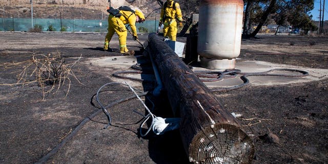 Firefighters with Cal Fire examine a burned down low voltage power pole during the Tick Fire, Thursday, Oct. 25, 2019, in Santa Clarita, Calif. An estimated 50,000 people were under evacuation orders in the Santa Clarita area north of Los Angeles as hot, dry Santa Ana winds howling at up to 50 mph (80 kph) drove the flames into neighborhoods (AP Photo/ Christian Monterrosa)