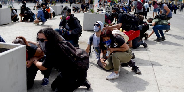 Anti-government protesters take cover just around the corner from the Congress building, during clashes with police in Valparaiso, Chile, Friday, Oct. 25, 2019. A new round of clashes broke out Friday as demonstrators returned to the streets, dissatisfied with economic concessions announced by the government in a bid to curb a week of deadly violence.(AP Photo/Matias Delacroix)