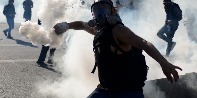 An anti-government protester returns a tear gas canister to police during clashes in Valparaiso, Chile, Friday, Oct. 25, 2019. A new round of clashes broke out Friday as demonstrators returned to the streets, dissatisfied with economic concessions announced by the government in a bid to curb a week of deadly violence.(AP Photo/Matias Delacroix)