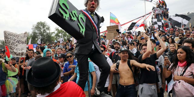 An artist performs as Chile's President Sebastian Pinera holding a briefcase embellished with dollars signs, during an anti-government protest in Santiago, Chile, Friday, Oct. 25, 2019. At least 19 people have died in the turmoil that has swept the South American nation. The unrest began as a protest over a 4-cent increase in subway fares and soon morphed into a larger movement over growing inequality in one of Latin America's wealthiest countries. (AP Photo/Rodrigo Abd)