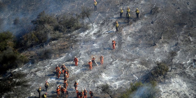 Hand crews work a wildfire-damaged hillside as the Getty fire burns on Mandeville Canyon, Oct. 28, 2019, in Los Angeles. (AP Photo/Marcio Jose Sanchez)