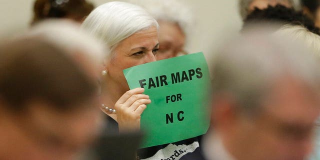 In this July 26, 2017 photo, a member of the gallery tried to display her sign while lawmakers conveneD during a joint select committee meeting on redistricting in Raleigh, N.C. North Carolina judges on Monday blocked the state's congressional map from being used in the 2020 elections. (AP Photo/Gerry Broome, File)