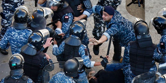 A riot police officer, center right, stops other policemen from beating a protester who lies on the ground, after clashes erupted between an anti-government protesters and Hezbollah supporters near the government palace, in Beirut, Lebanon, Tuesday, Oct. 29, 2019.
