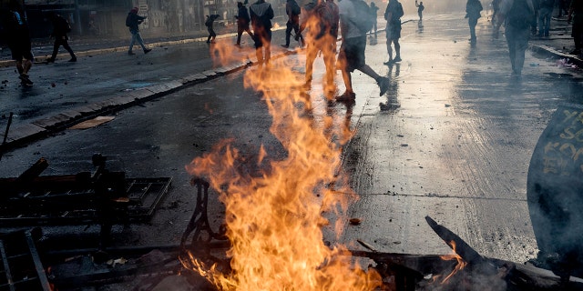Anti-government protesters walk past a burning barricade set fire by protesters during clashes with police in Santiago, Chile, Tuesday, Oct. 29, 2019. (AP Photo/Rodrigo Abd)