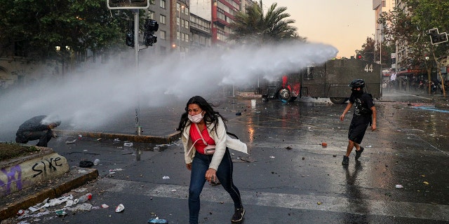 An anti-government protester walks away from the spray of a police water cannon in Santiago, Chile, Tuesday, Oct. 29, 2019.